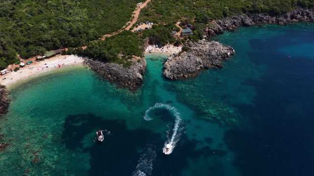 Aerial view of Aquarium Bay with turquoise waters, rocky cliffs, and a boat making a wake in Himara, Qarku i Vlores, Albania.