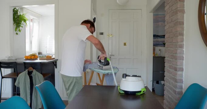 Man Steaming a Shirt in a Dining Room: A man in a white t-shirt and shorts, wearing a snorkel and mask, humorously attempts to steam a shirt using a handheld steamer in a bright dining room.