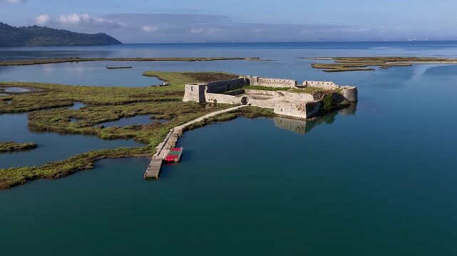 Aerial view of Ali Pasha Castle surrounded by marshland and calm water with a small pier in Mahala, Qarku i Vlores, Albania.
