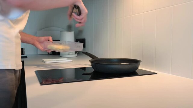 Woman takes a prepared filling out of a container and places crepes on a pan to fry. She cooks stuffed pancakes on an induction stove in her home kitchen. Concept of home cooking, breakfast