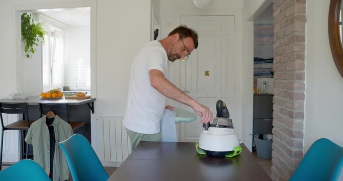 Man Vacuuming Dining Table: A man in casual attire is diligently vacuuming crumbs and debris from a dark wooden dining table, demonstrating a commitment to a clean and orderly home environment.