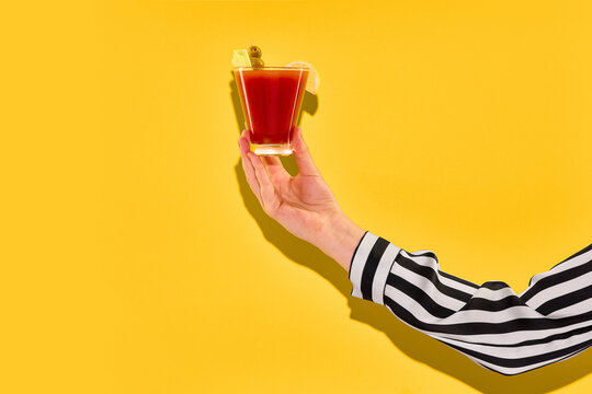 Hand holding red cocktail on yellow background. Concept of cocktail bar menu, nightlife drinks, beverage advertising, brunch culture, and social media content.