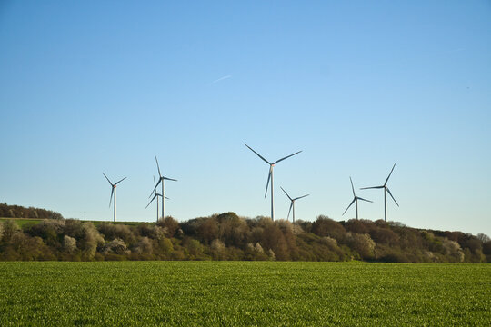 Modern wind turbines on a hill behind a green field.