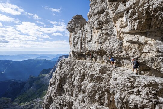 Three mountaineers on an exposed rock band in the secured via ferrata Bocciere Centrale, Brenta Mountains, Brenta-Adamello Natural Park, Trentino, Italy