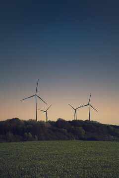 Wind turbines as silhouettes on a hill at twilight.
