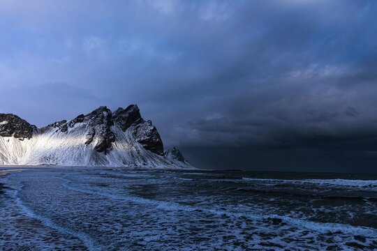 White foamy waves on the beach of Stokkness, behind snowy rocky slopes of Vestrahorn, near H&ouml;fn, Sudausturland, Iceland