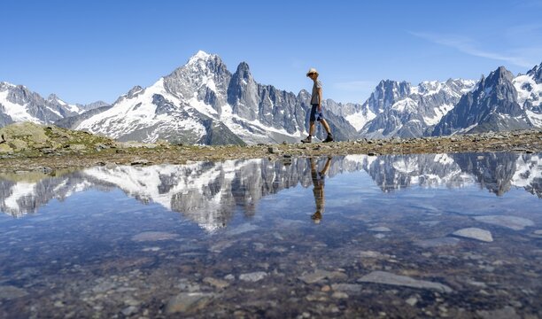 Tourist in front of mountain landscape, reflection in a small mountain lake, mountain peaks Aiguille Verte and Grandes Jorasses, mountain panorama with Mont Blanc massif, Aiguille Rouge, Chamonix-Mont-Blanc, Haute-Savoie, France