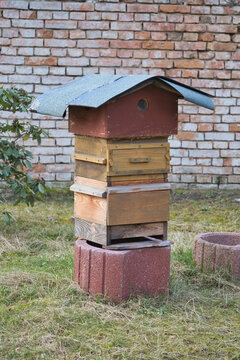 A Traditional Stacked Wooden Beehive Standing Before a Rustic Brick Wall