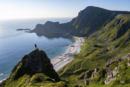 Climber on a rock, view of picturesque coastal landscape, steep coast with peak M&aring;tind or M&aring;tinden, H&oslash;yvika beach and sea, hike to the summit of M&aring;tind, And&oslash;ya island, Vester&aring;len, Nordland, Norway