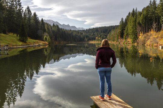 Female hiker stands on a footbridge and looks across the lake, autumn at Grubsee, near Kr&uuml;n, Karwendel, Upper Bavaria, Bavaria, Germany