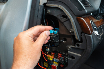 Fototapeta premium Mechanic hand removing a car fuse from the vehicle fuse box. Close-up of replacing a burnt automotive electrical fuse.
