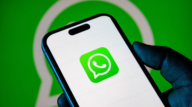 Smartphone displaying the whatsapp application logo on the screen held in hand against a green background