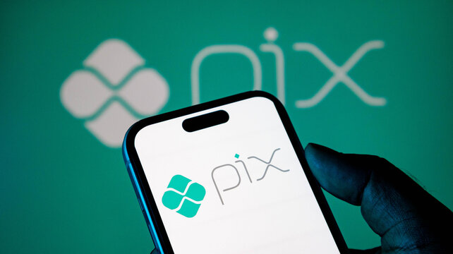 Closeup of a smartphone screen displaying the pix payment system logo, held by a person against a green background with the pix logo