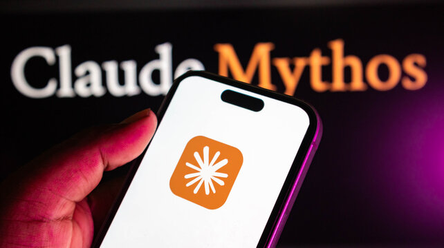 Closeup of a hand holding a smartphone displaying a claude  app icon with a white starburst symbol against a blurred background with the text claude mythos