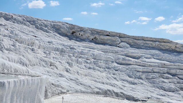 Stunning view of Pamukkale&rsquo;s white travertine terraces from below, illuminated by bright sunlight under a clear blue sky. Perfect travel and nature landscape.