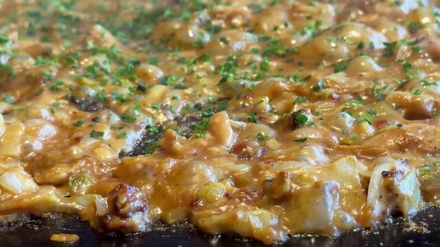 日本のもんじゃ焼き。鉄板焼き料理。キャベツや鶏肉で作るカレー味のもんじゃの動画。クローズアップ。