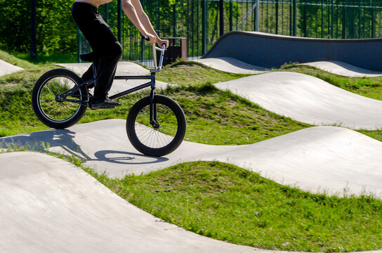 teen rides bmx bike on concrete pump track with grassy hills. this track provides fun sport and rest for youth. modern track blends eco-friendly design with active outdoor recreation.