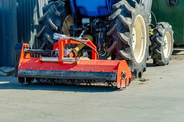 red tiller is attached to blue tractor for soil preparation. this tiller helps farmers plow ground efficiently. modern tiller ensures high quality agricultural work in outdoor farm environment © Ninaveter
