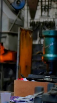 Vertical video: Panning camera showing box with tools on bench at shop, revealing forge, copy space
