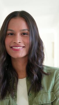 Vertical video: Camera zooming in to connect woman uncrossing arms, smiling at home in green jacket