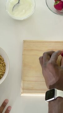 Vertical video: Right hand entering lifting berry removing top on home counter for bowl, copy space