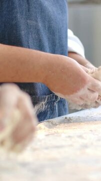 Vertical video: Shaping dough at start, denim-apron baker forming loaf on floured bench for baking