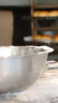 Vertical video: Reaching forearm in white sleeve pulling flour from steel bowl at bakery, for dough