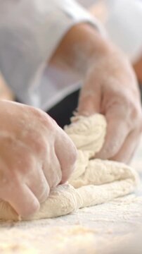 Vertical video: Pressing chef hands folding shaping ball placed on floured worktop, with white cuff