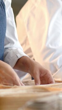 Vertical video: Picking dough baker pinching and folding to proof at bakery, bannetons white coat