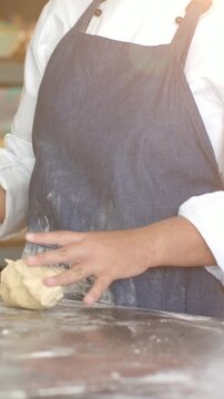 Vertical video: Lifting dough, chef in jacket and apron shaping at bakery counter checking tablet
