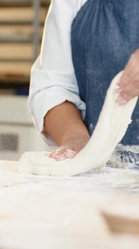 Vertical video: Picking up dough baker in white coat and blue apron shaping at bakery for proofing