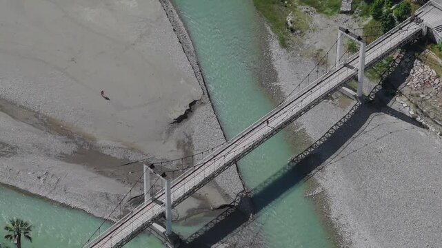 Aerial view of a suspension footbridge over the turquoise Osum River with people walking across the deck in Berat, Berat County, Albania.