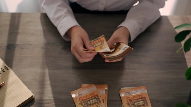 Woman in white shirt counting and organizing euro banknotes into stacks at office desk, performing accounting work and financial record management in business environment.Accounting, bookkeeping