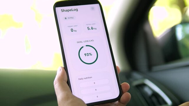 Clean mobile UI design displaying a weight goal ring. Hand holding phone in a car interior. Great for app showcases, software development, and health tech promotional footage.