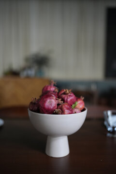 Fresh ripe pomegranates in a modern white ceramic bowl on a wooden table, cozy stylish kitchen blurred interior background