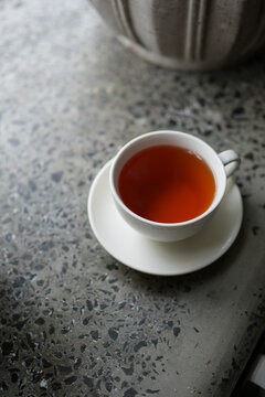 High angle shot of steaming freshly brewed black or herbal tea in a classic white teacup on a textured concrete tabletop. Relaxing break time concept