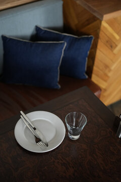 High angle shot of a clean white ceramic plate with cutlery and an empty glass on a natural wood dining table. Ready for serving in a cozy modern restaurant