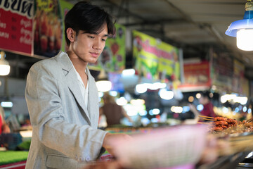 Naklejka premium Serious young nonbinary Thai business professional shopping at street food night market