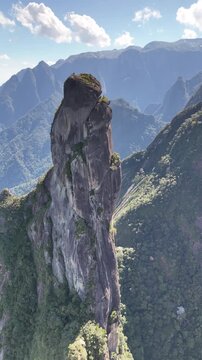 Wide aerial shot of Dedo de Deus peak framed by rolling mountain ridges and Atlantic Forest vegetation.