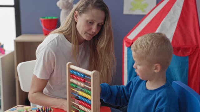 Teacher guiding young boy with abacus in school building, leaning close and smiling while pointing colorful beads; warmth learning trust.