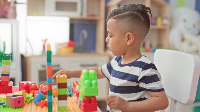 Little boy stacking colorful blocks with his hand at a playroom table in a building; imaginative play concentration.