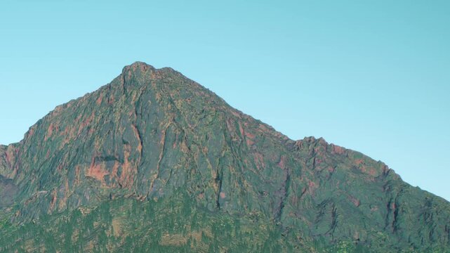 The view shows a mountain peak with a rocky surface and clear blue sky above. The scene captures the natural beauty of the landscape in bright daylight.