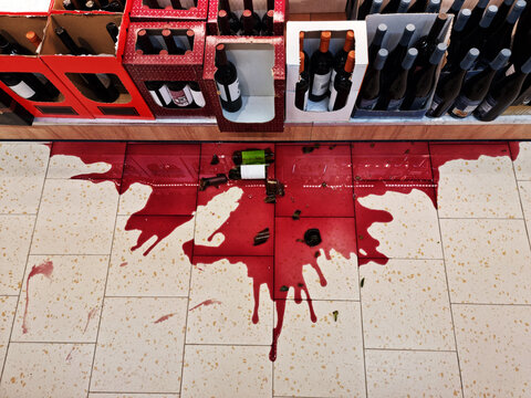 Broken bottle of red wine spilled on a store tile floor.