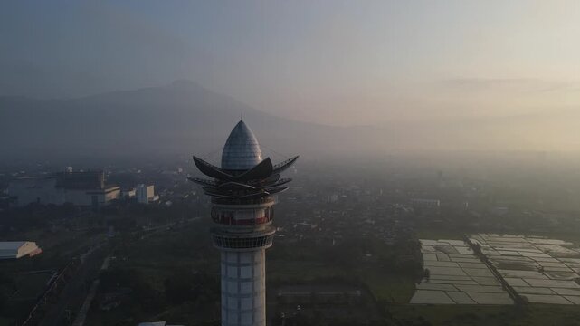 Aerial view of Menara Pandang Teratai lotus tower rising above the misty morning landscape with mountains in the background in Kecamatan Purwokerto Timur, Jawa Tengah, Indonesia.