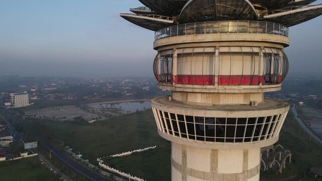 Aerial view of the modern Menara Pandang Teratai observation tower overlooking the urban landscape and green fields in Kecamatan Purwokerto Timur, Jawa Tengah, Indonesia.