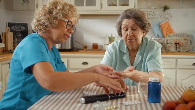 Caregiver encourages a senior woman to take her medication at home while offering patient support and compassionate care during her daily treatment routine.
