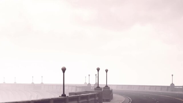 A long road stretches into the distance under a layer of fog. Streetlights line the sides of the road, creating a quiet and empty scene.