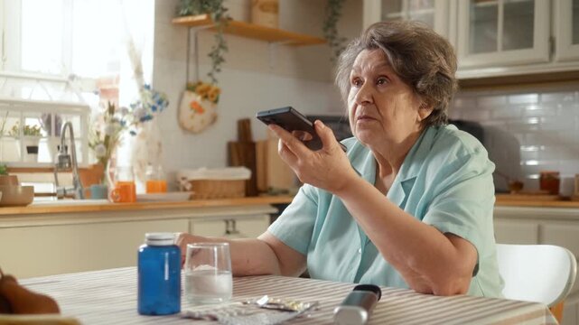 Senior woman uses a voice AI assistant on smartphone to check her medication schedule at home, showing digital health support for older adults.