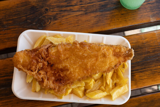 Fried fish served on a tray with golden chips in a casual dining setting at a seaside restaurant during the afternoon