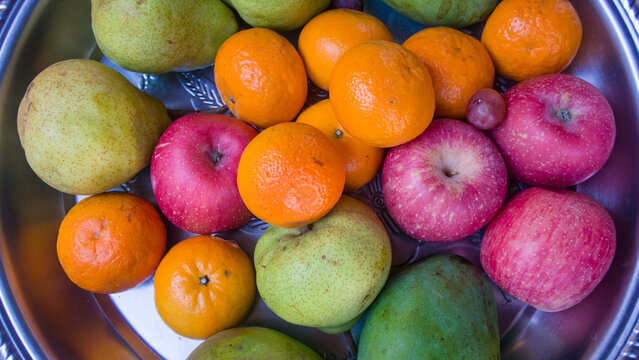 Top view of a silver platter filled with a colorful assortment of fresh apples, oranges, pears, and mangoes